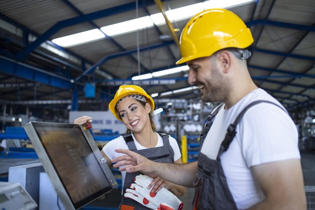 Factory-worker-explaining-trainee-how-operate-industrial-machine-using-new-software-touch-screen-computer